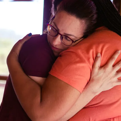 Duas alunas num abraço demorado, de olhos fechados