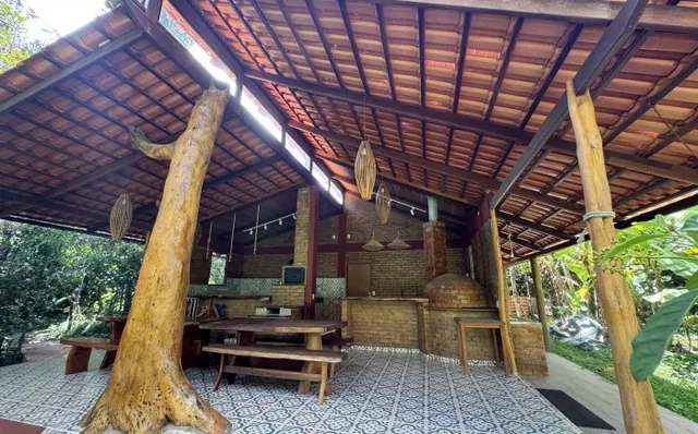 Área coberta de convivência com mesa comprida de madeira e forno