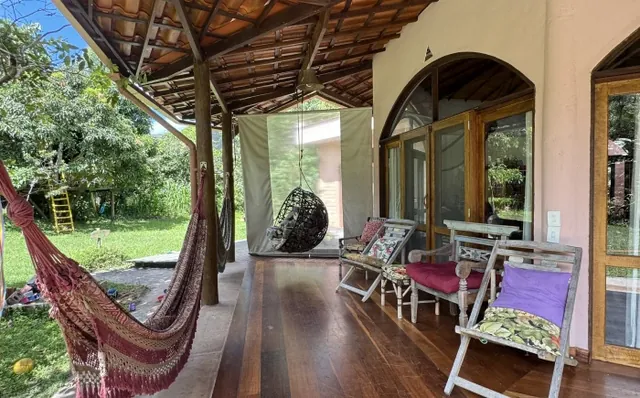 Varanda com rede, cadeira suspensa e poltronas, aberta para o jardim